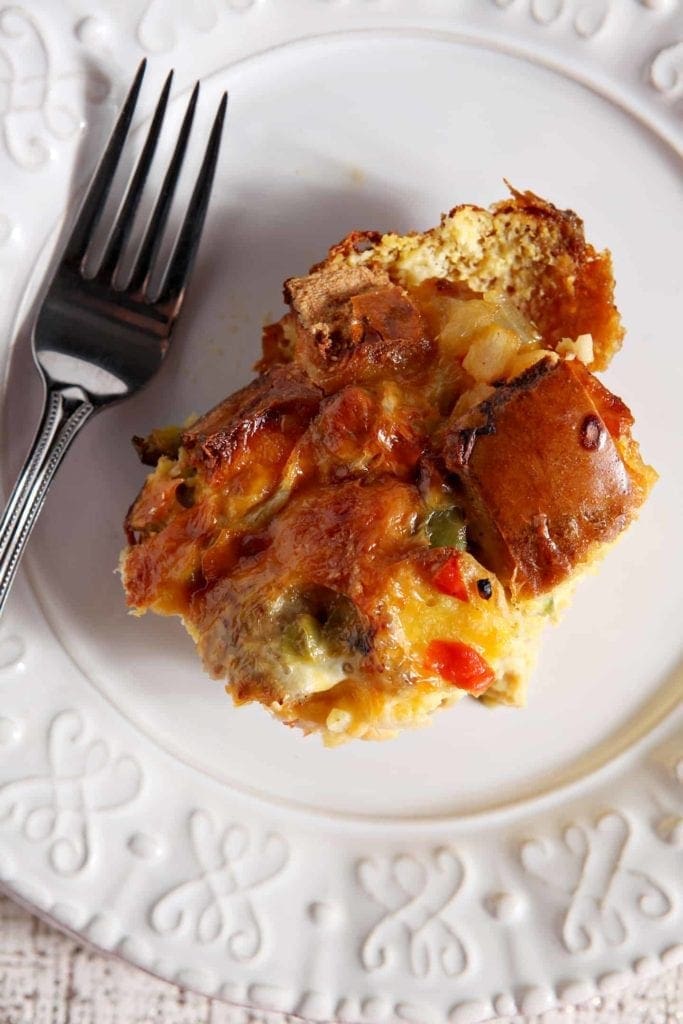 Close up of a serving of Christmas Breakfast Casserole on a white plate with a fork, shown from above