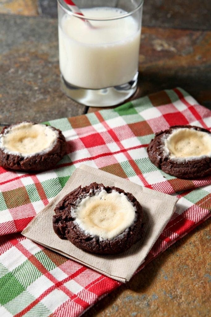 Three cookies on napkins and linens next to glass of milk