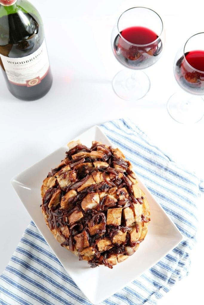 Overhead view of French Onion Bread in dish paired with glasses of red wine 