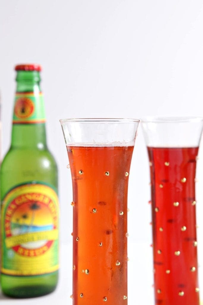 Close up of two glasses of ginger pomegranate drinks next to bottle