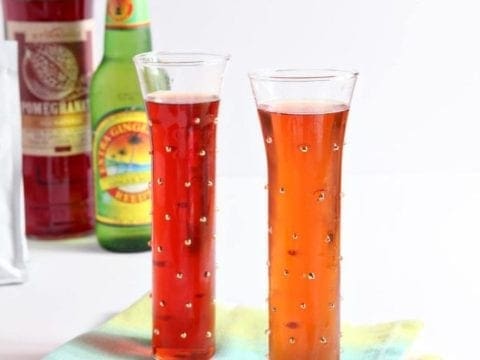 Two glasses of ginger pomegranate experiment drinks in front of bottles