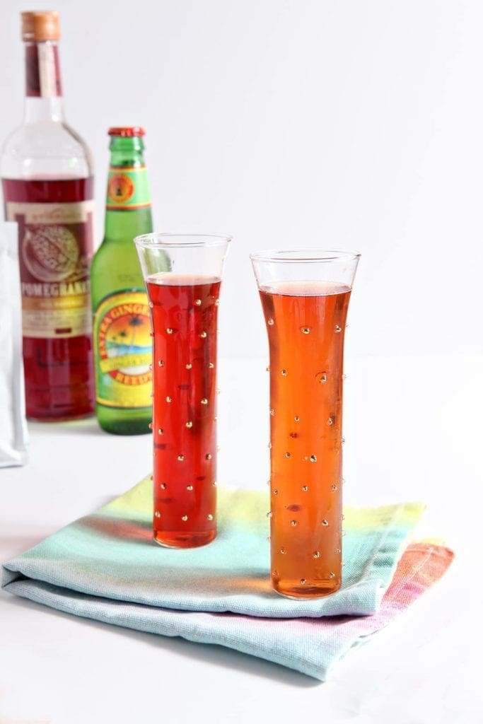 Two glasses of ginger pomegranate experiment drinks in front of bottles