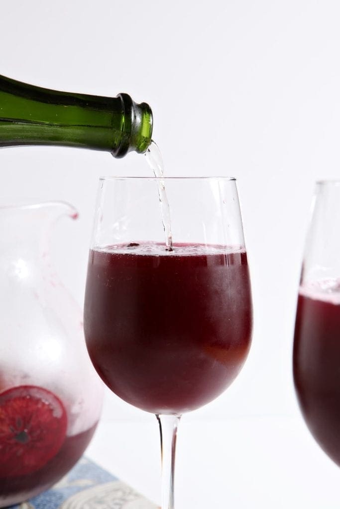 Bottle pouring Champagne in wine glass filled with sangria