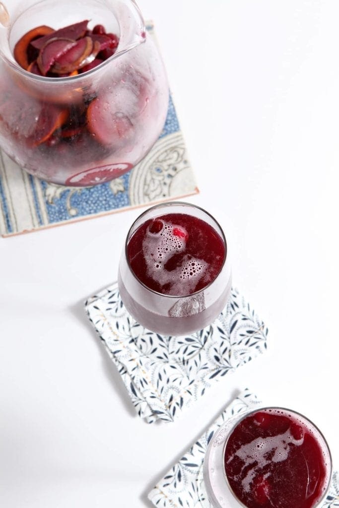 Two glasses of Winter Sparkling Champagne Sangria are served next to a pitcher holding the drink