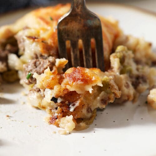 A fork delves into a plate of cottage pie topped with cheesy potatoes