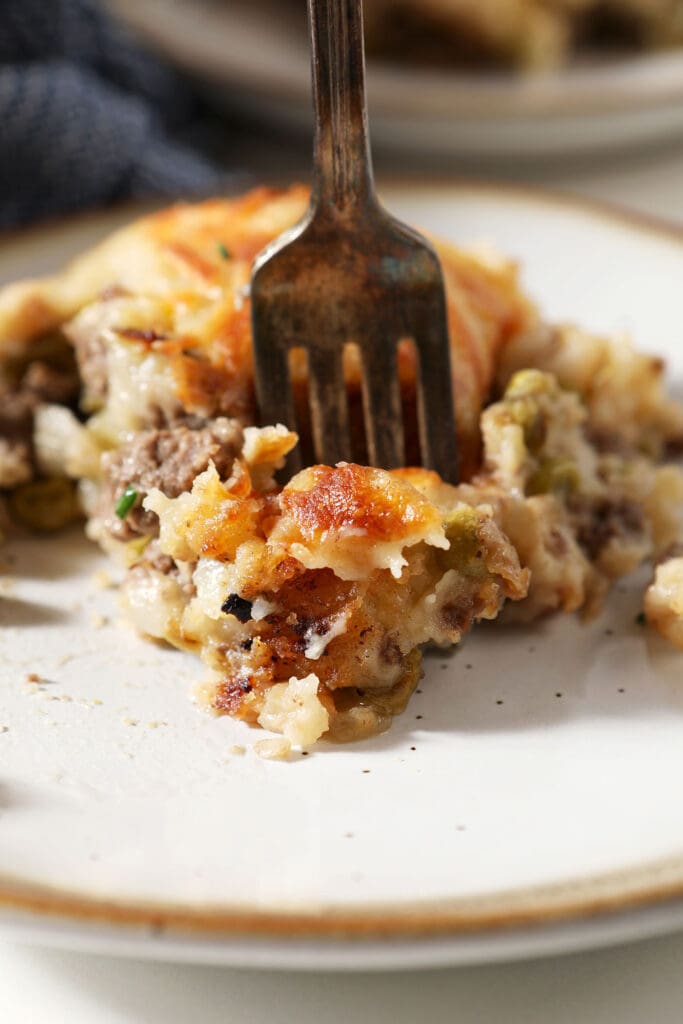 A fork delves into a plate of cottage pie topped with cheesy potatoes