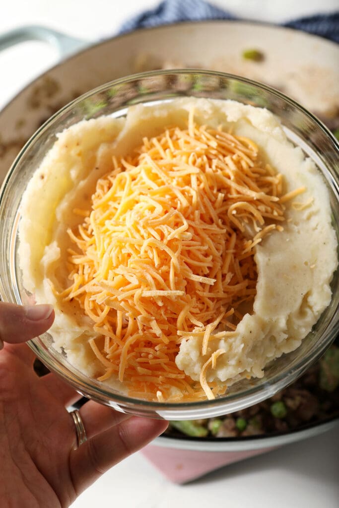 Shredded cheese on top of a bowl of roasted garlic potatoes