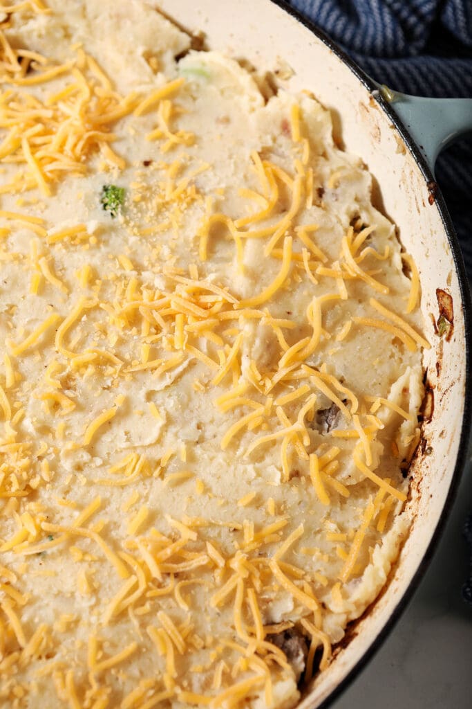 Shredded cheese on top of mashed potatoes on a cottage pie before baking