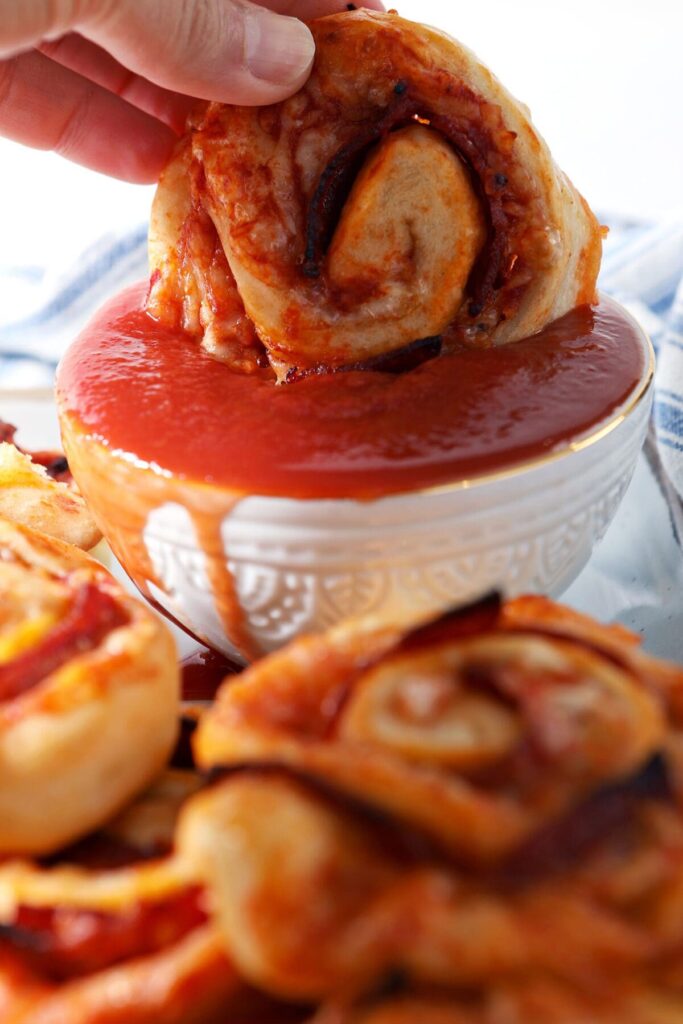 A pepperoni pizza roll dunks into a bowl of pizza sauce