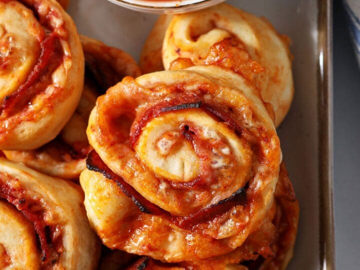A platter of pepperoni pizza rolls with a bowl of pizza sauce