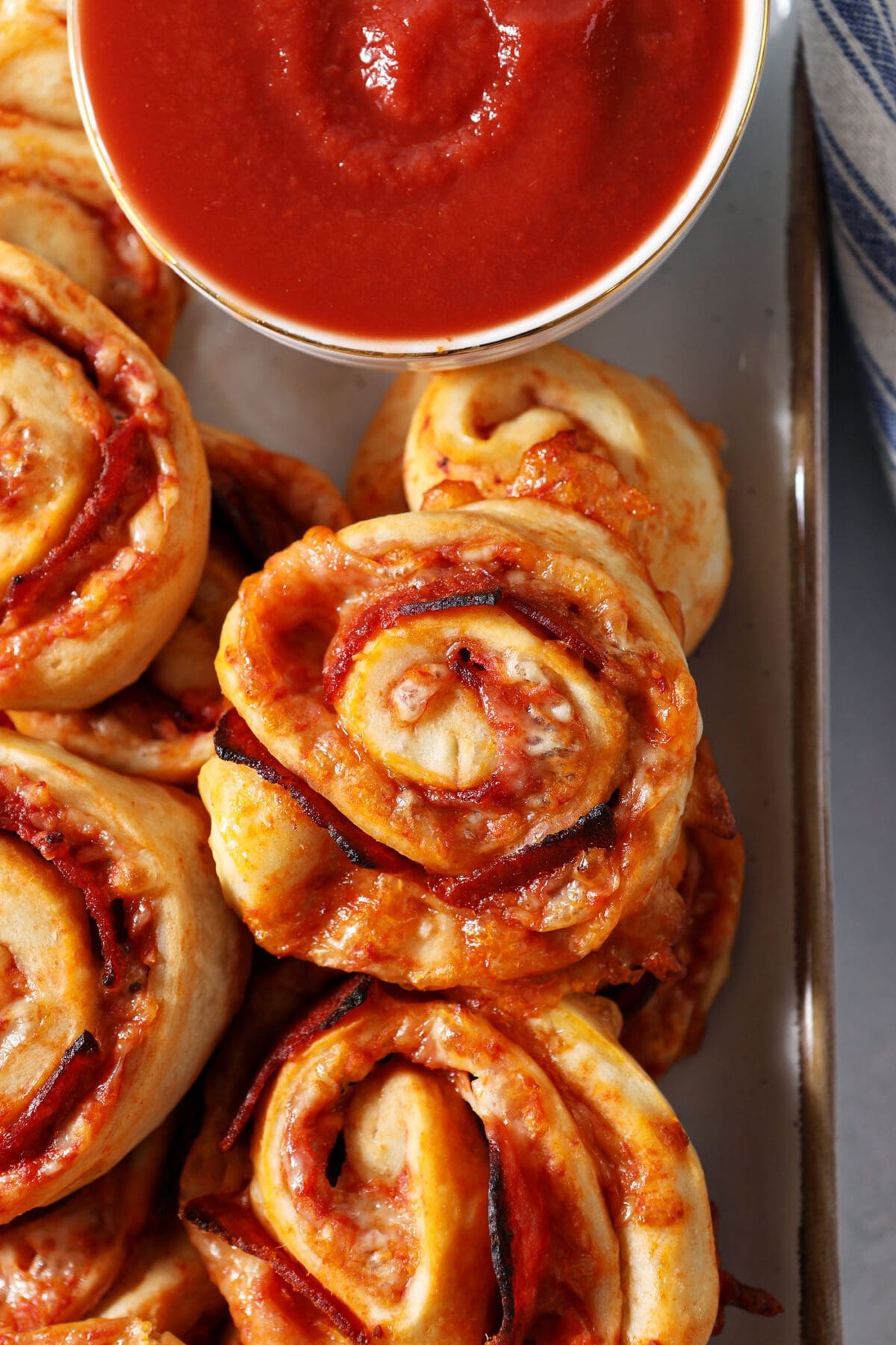 A platter of pepperoni pizza rolls with a bowl of pizza sauce