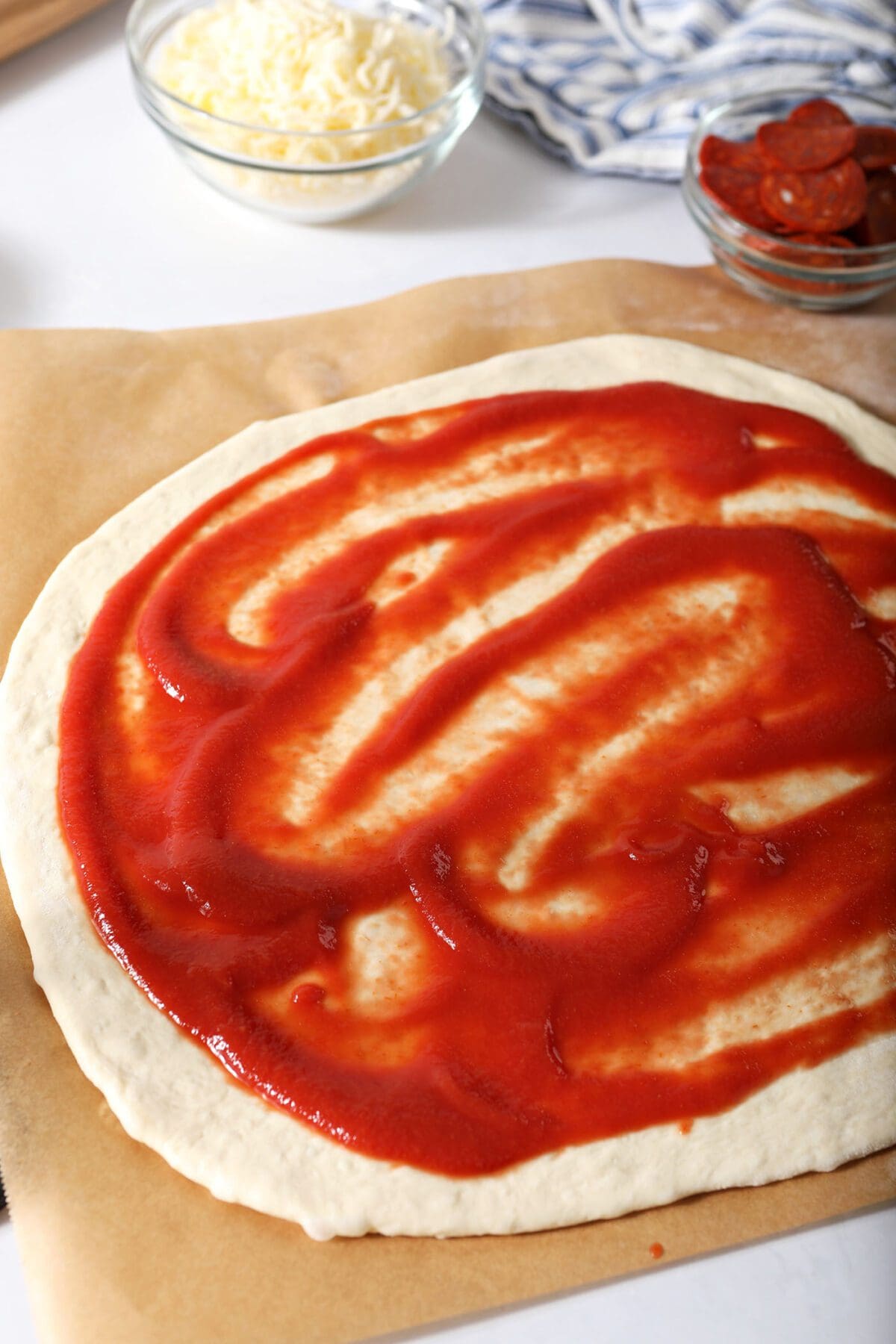 Pizza sauce is slathered on top of rolled out pizza dough