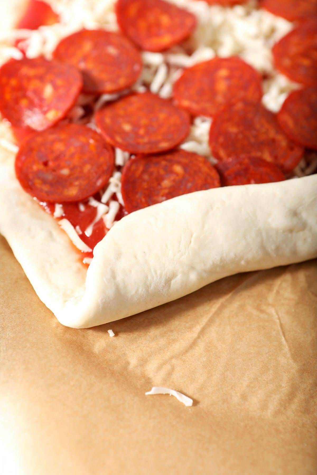 The edge of the pizza dough is curled over, beginning to roll the pizza rolls