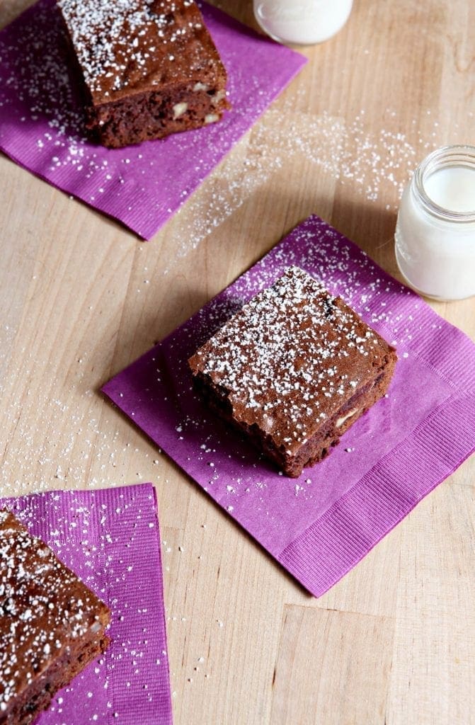 Bourbon Pecan Brownies, served on a wooden platter on purple napkins, with mini glasses of milk. 