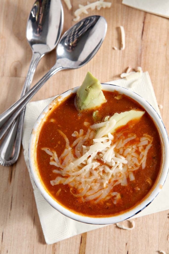 Close up of a bowl of taco soup with cheese and avocado slices