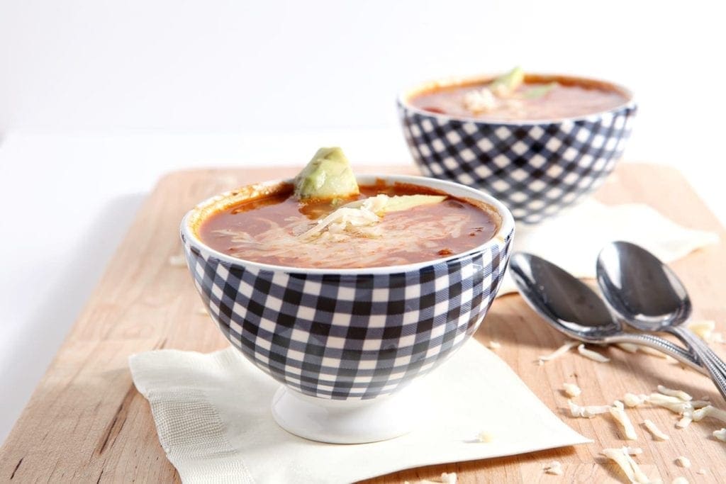 Two bowls of taco soup with spoons and cheese on wood