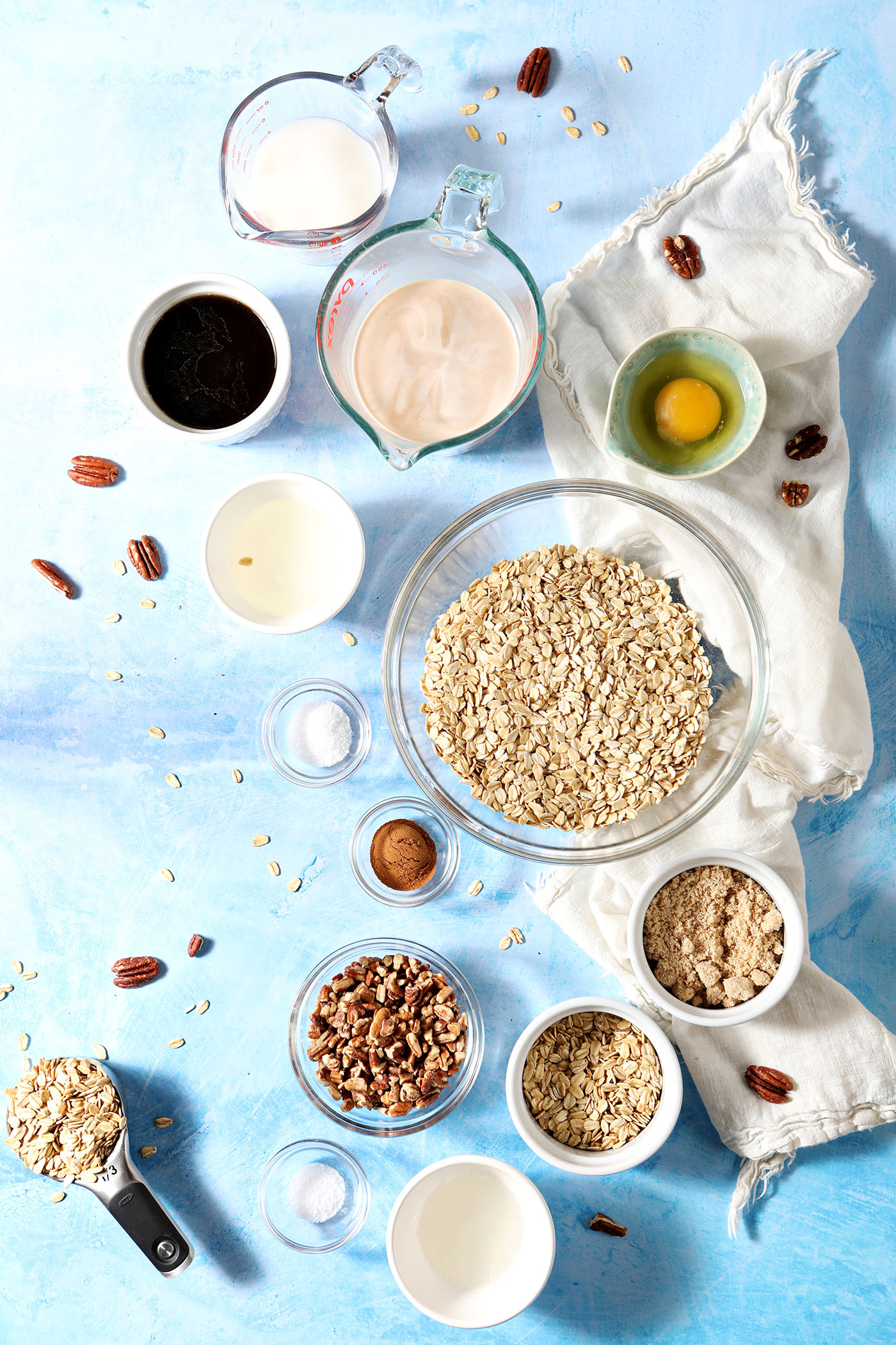 Ingredients to make Baked Oatmeal with Pecan Streusel in bowls on a blue surface with a white linen