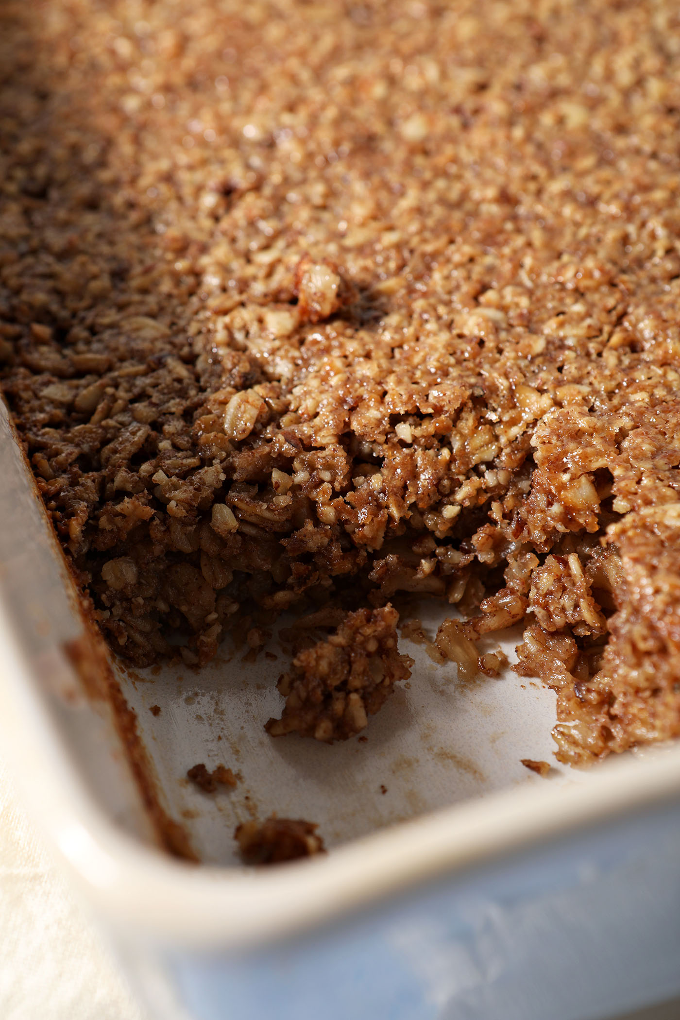 A close up of a sliced-into baked oatmeal with a pecan streusel in a casserole dish