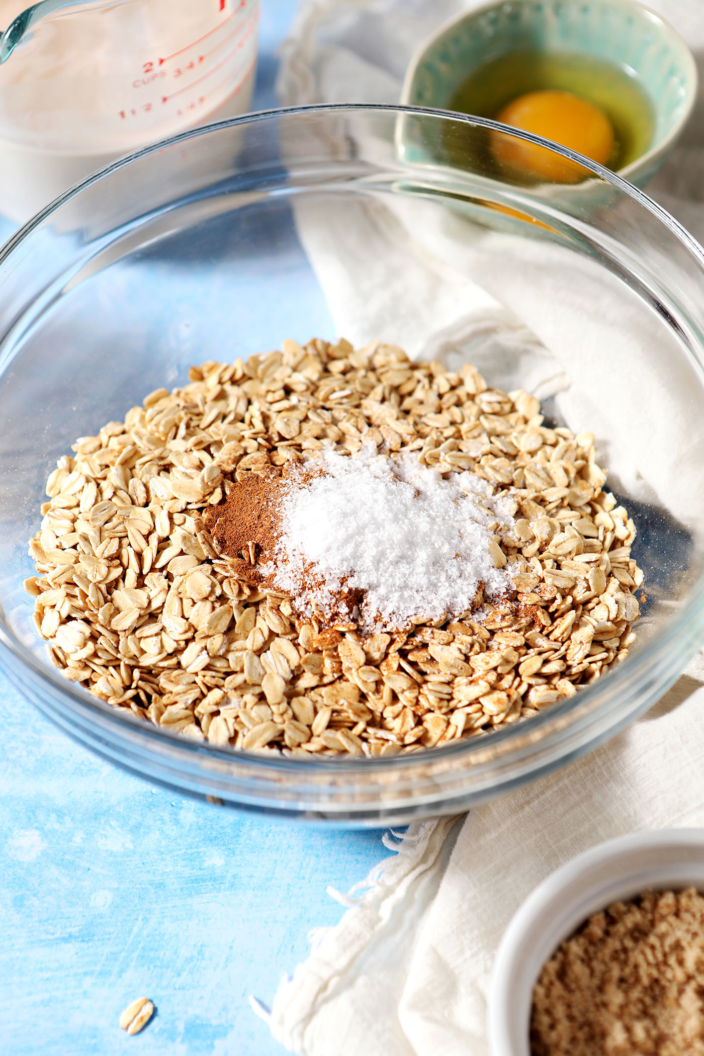 Oats in a bowl with seasonings before mixing on a blue surface