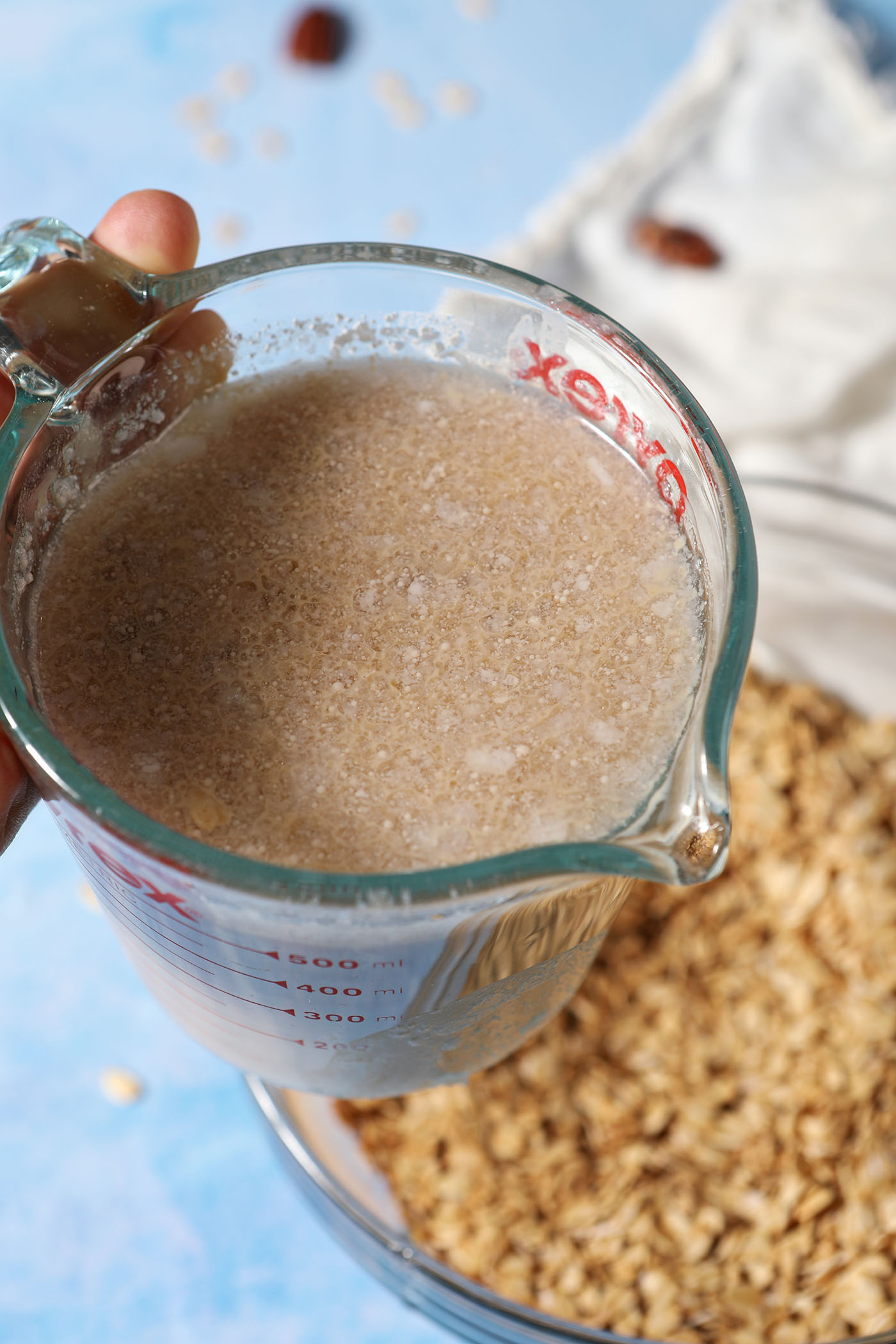 Wet ingredients in a glass measuring cup above a bowl of oats before pouring