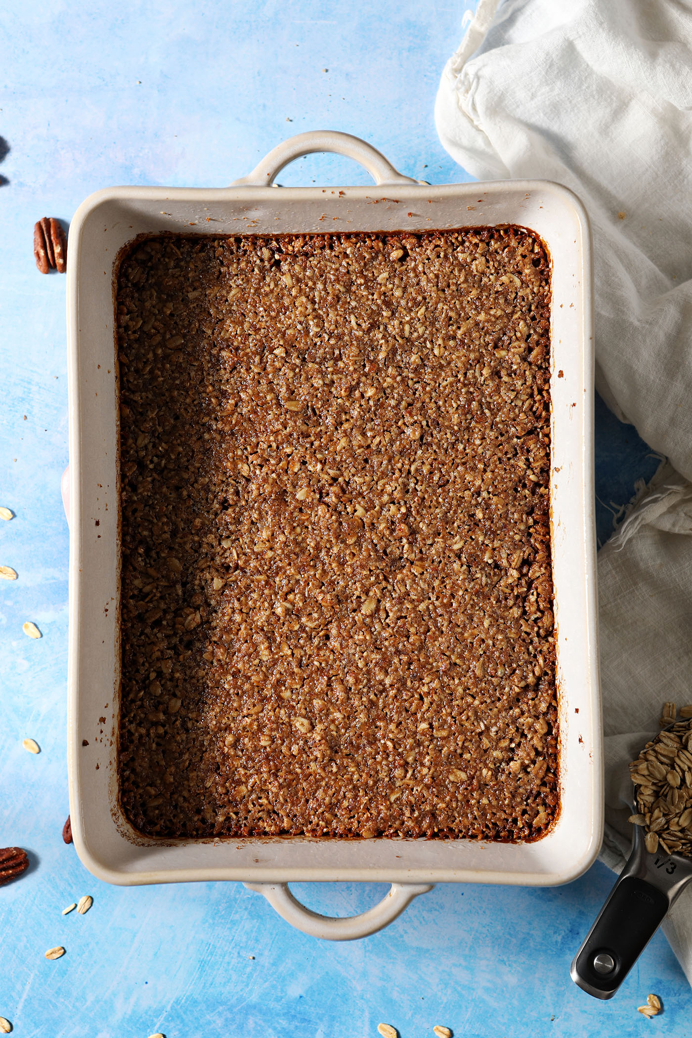 A Baked Oatmeal with Pecan Streusel in a casserole dish on a blue surface next to a white linen