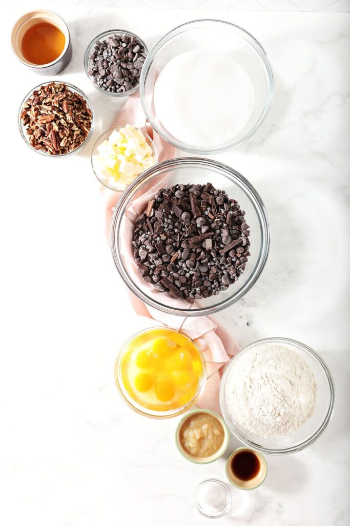 Ingredients to make chocolate chip brownies in bowls on marble