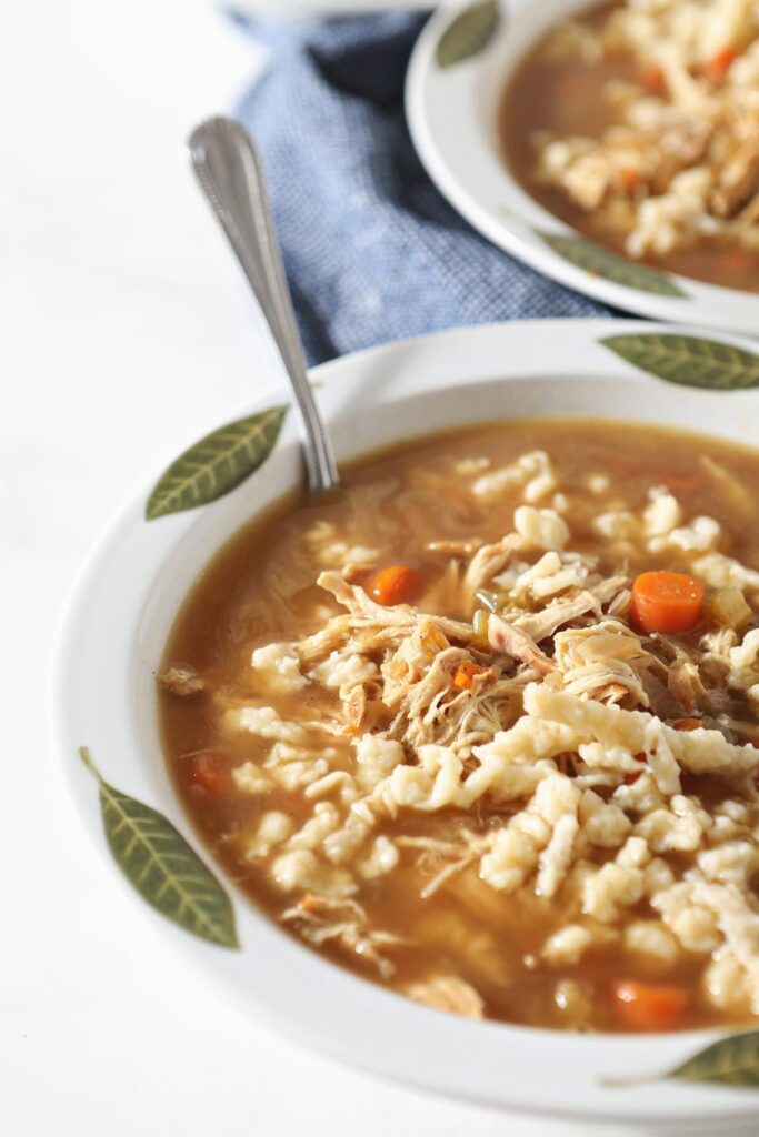 Close up of a bowl of chicken soup with German noodles on marble with a spoon in it