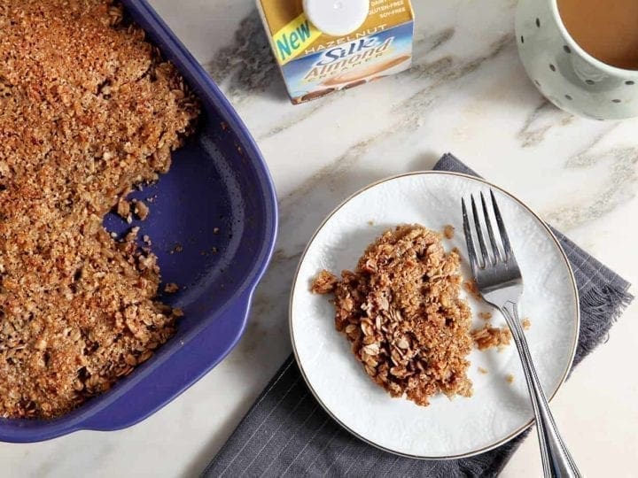A helping of Hazelnut and Pecan Baked Oatmeal is shown on a white plate with the baking dish of oatmeal and Silk Almond Milk Creamer.