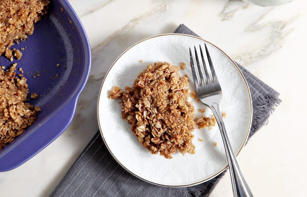 A serving of Baked Oatmeal with Hazelnut and Pecans on a white plate next to a purple casserole dish