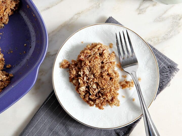 A serving of Baked Oatmeal with Hazelnut and Pecans on a white plate next to a purple casserole dish