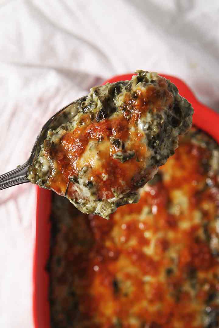 A large spoon holds a scoop of baked Spinach Madeline