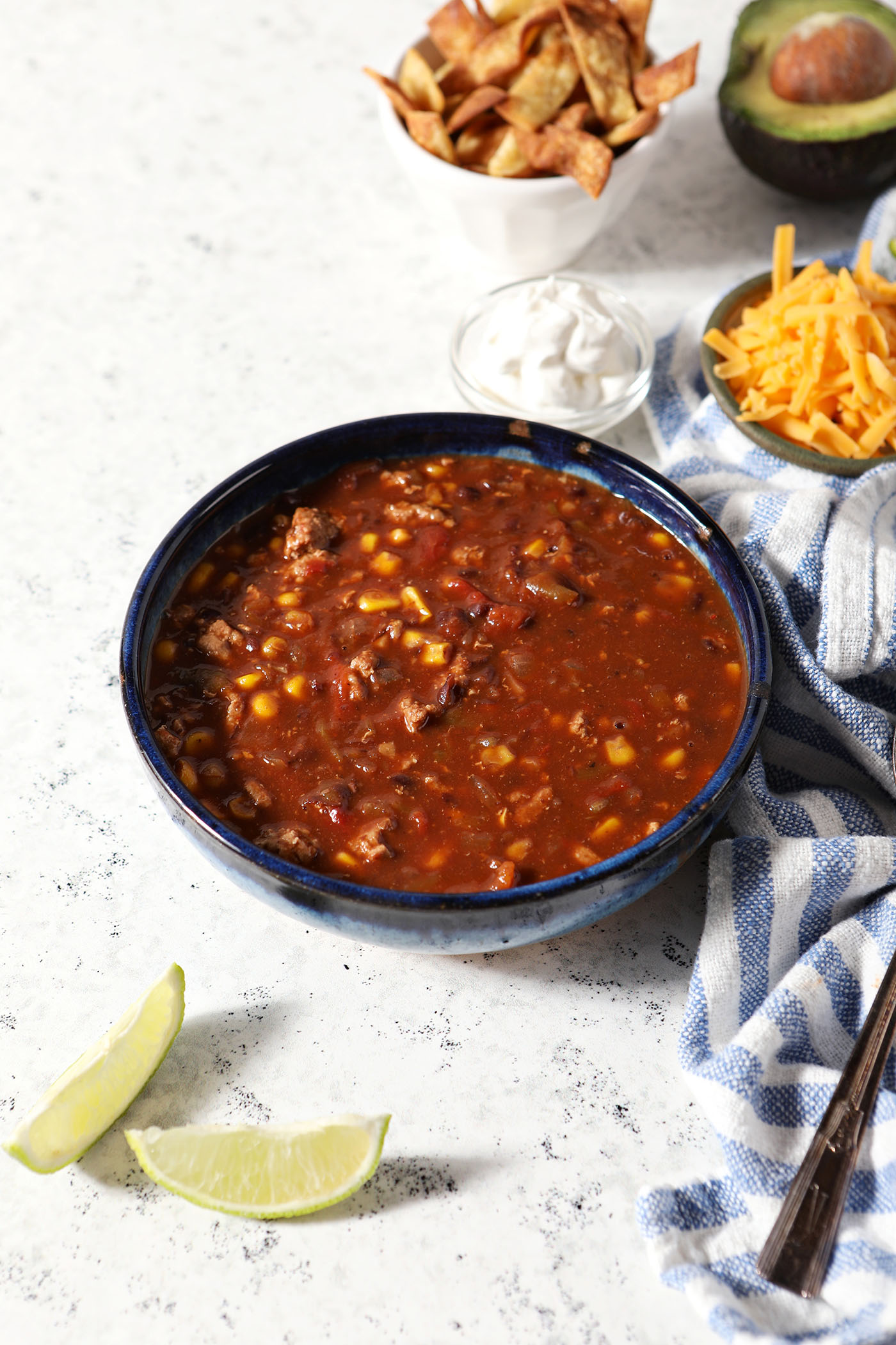 A bowl of Ground Turkey Taco Soup on a marble surface surrounded by toppings in bowls and a blue and white linen