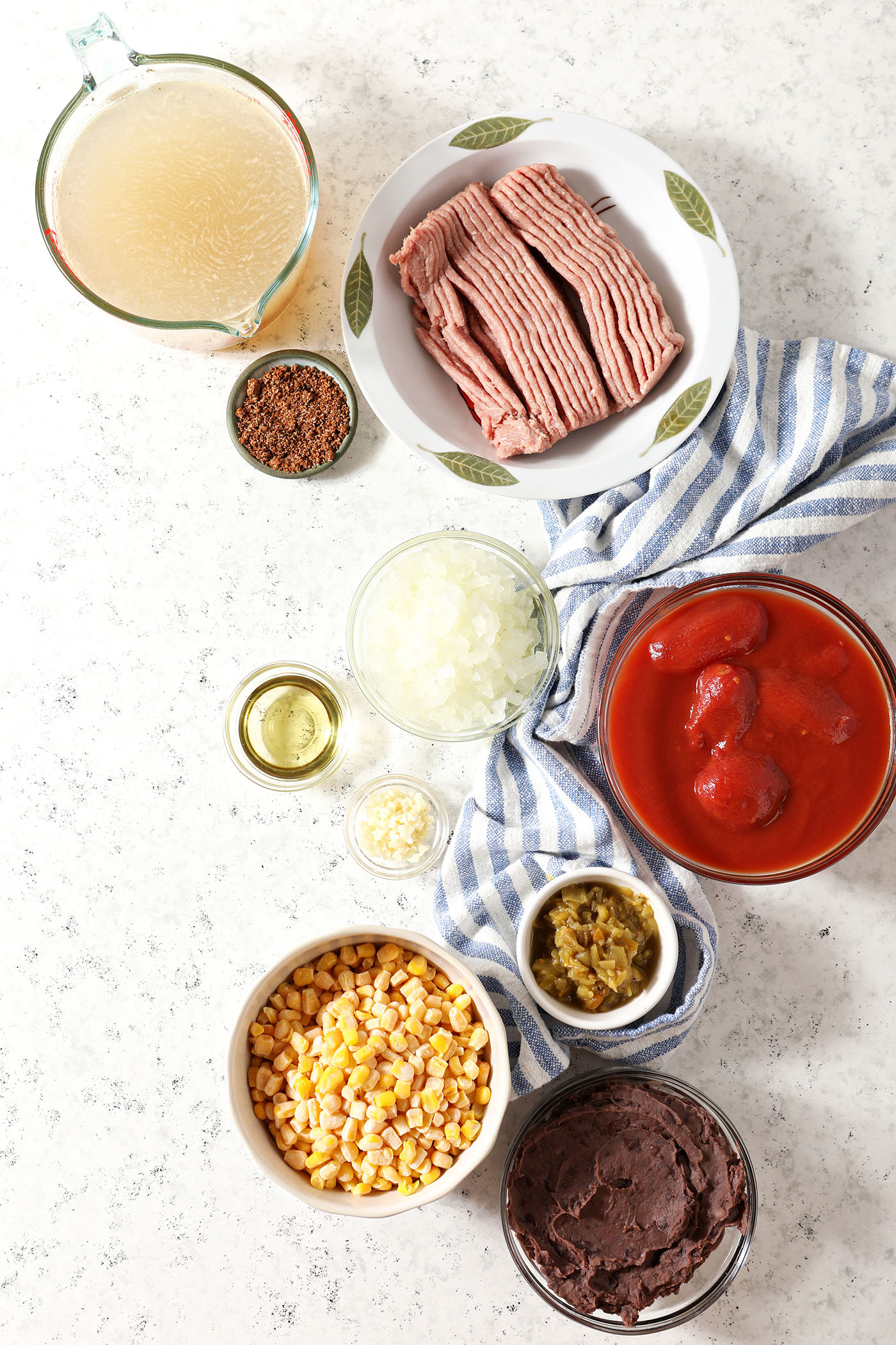 Ingredients to make taco soup with ground turkey in bowls on a marble surface with a blue and white linen
