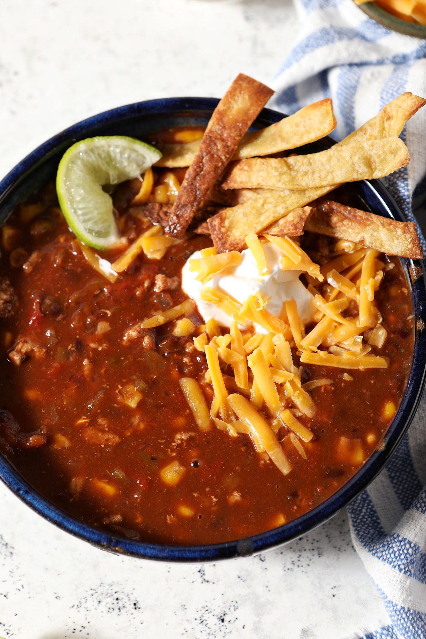 Close up overhead of a bowl of Turkey Taco Soup garnished with tortilla strips, a lime wedge, sour cream and shredded cheese