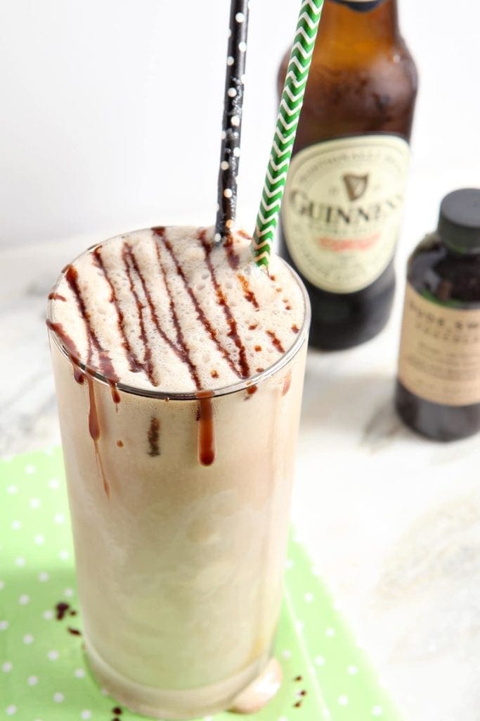 A Salted Caramel Guinness Float sits on top of a light green napkin in front of a beer bottle and a bottle of chocolate sauce