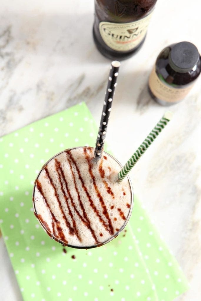 Overhead of a beer float drizzled with chocolate with straws in it on a light green napkin