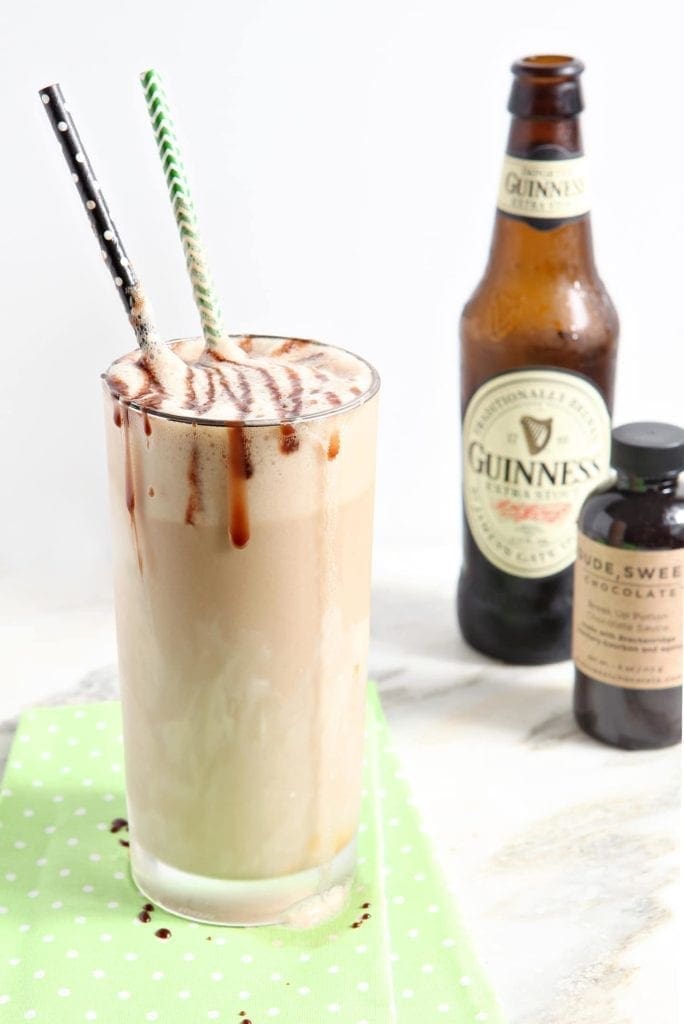 A Salted Caramel Guinness Float sits on top of a light green napkin in front of a beer bottle and a bottle of chocolate sauce