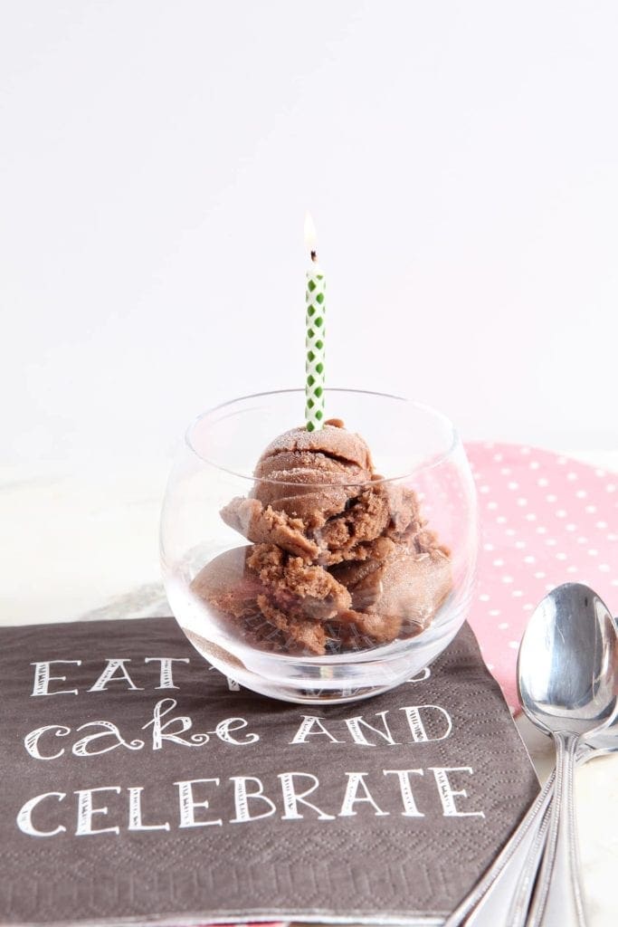 Scoops of chocolate banana ice cream in glass with lit birthday candle 