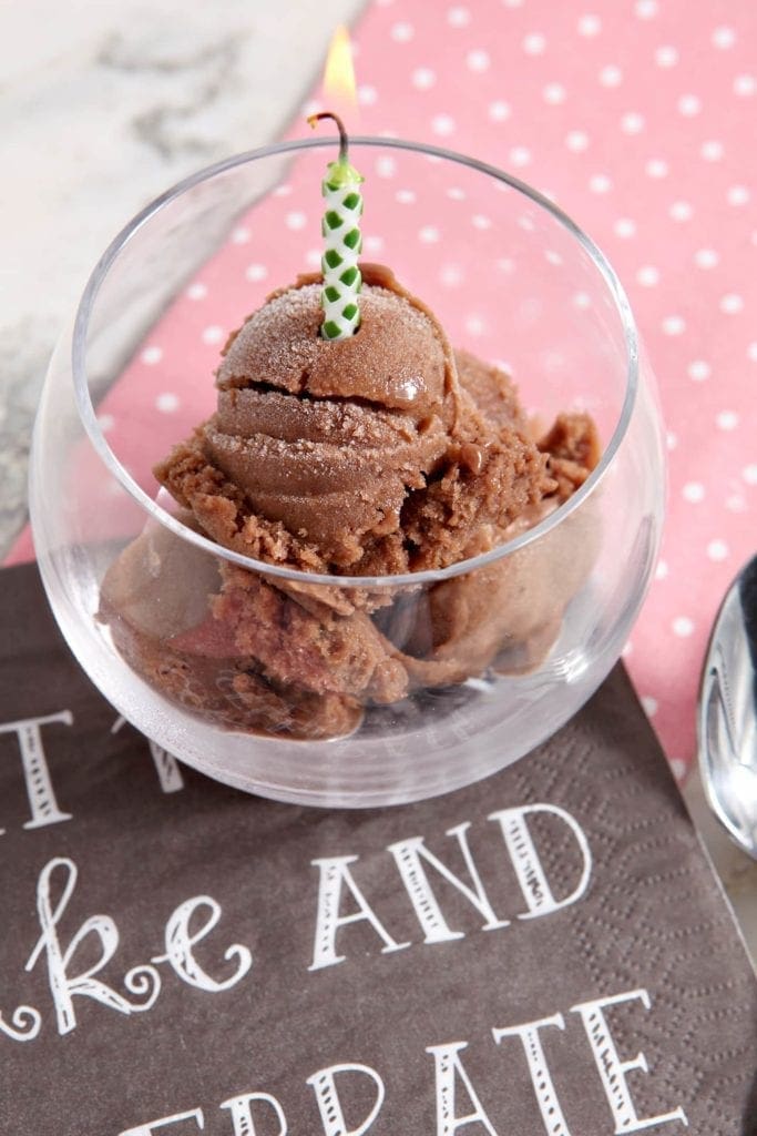 Overhead angled view of chocolate banana ice cream in glass with lit candle 