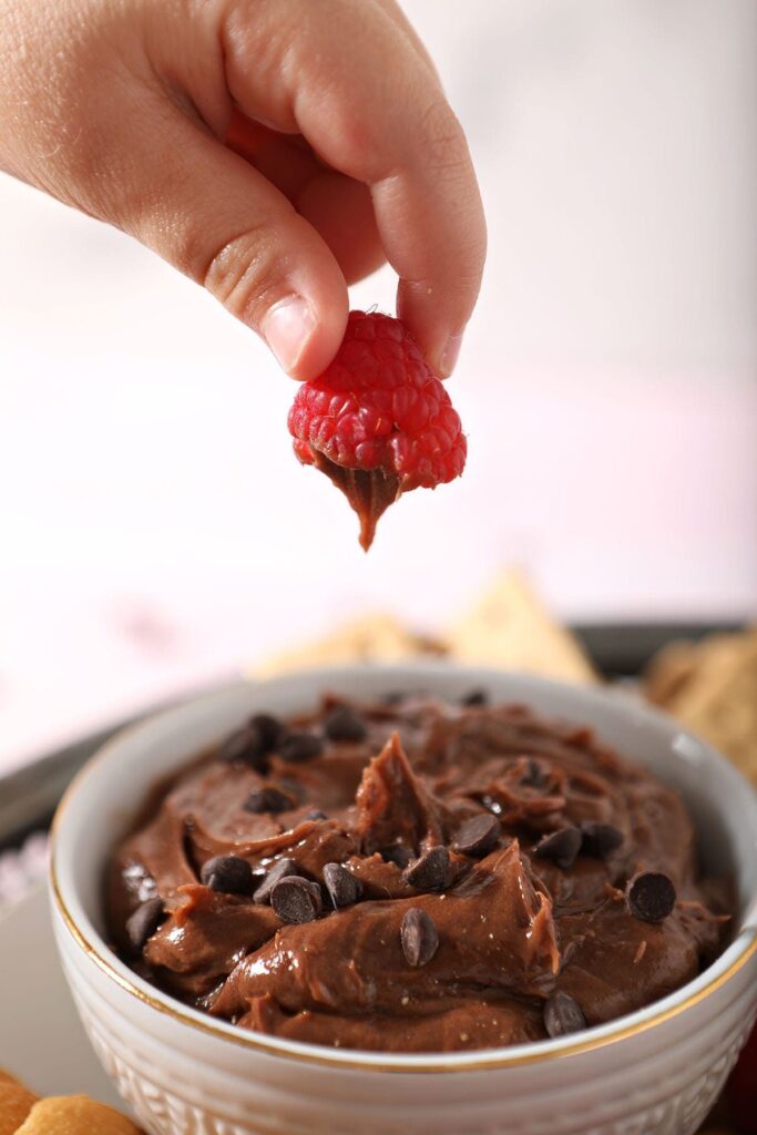 A child pulls a raspberry out of chocolate dip