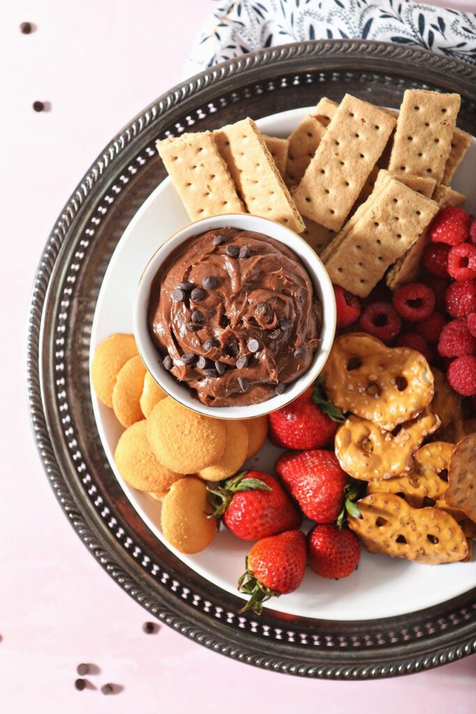 A platter holding chocolate fruit dip surrounded by crackers, fruit and cookies