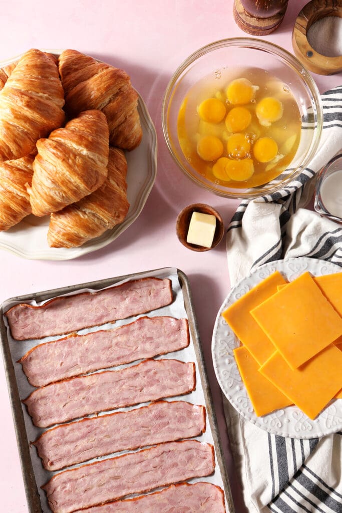 ingredients to make breakfast sandwiches with croissants with the eggs and bacon uncooked