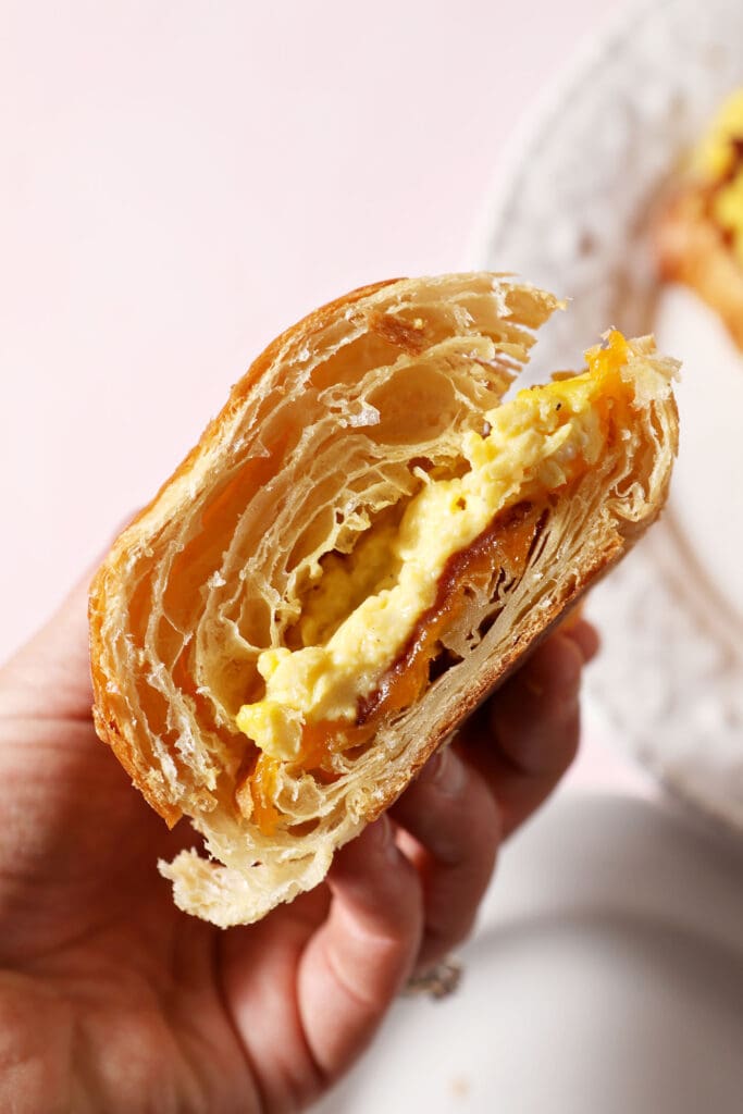 a halved croissant breakfast sandwich held in hand above a pink surface