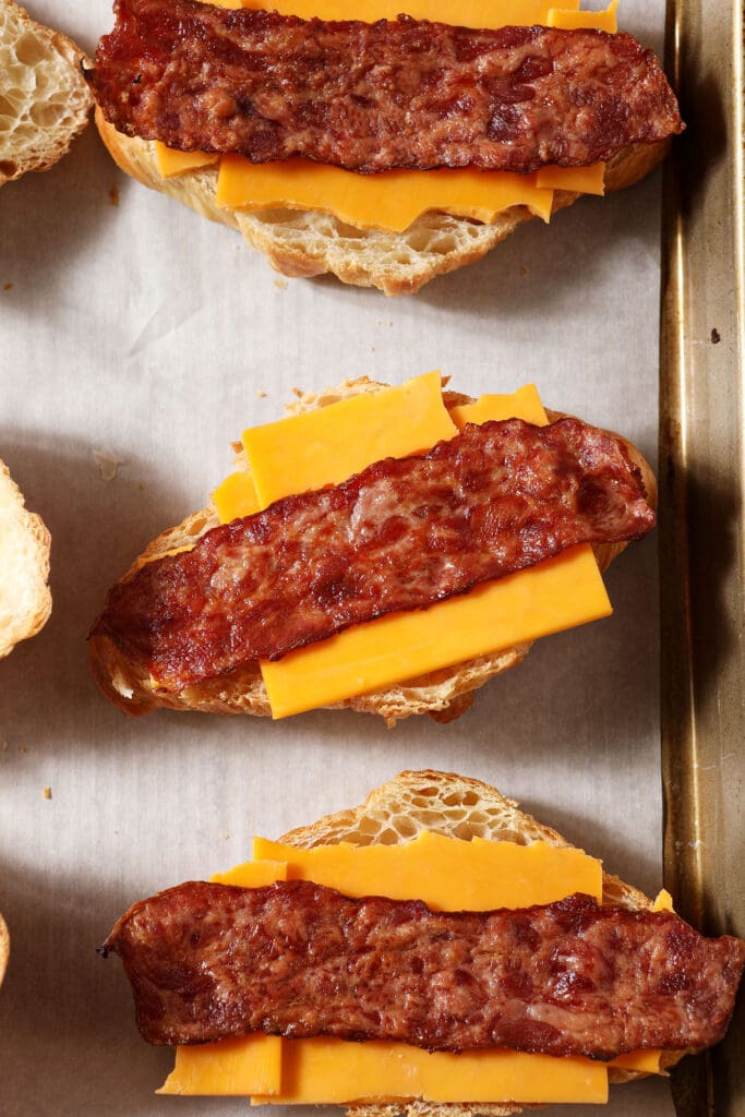 bacon sits on top of cheese on croissants on a sheet pan