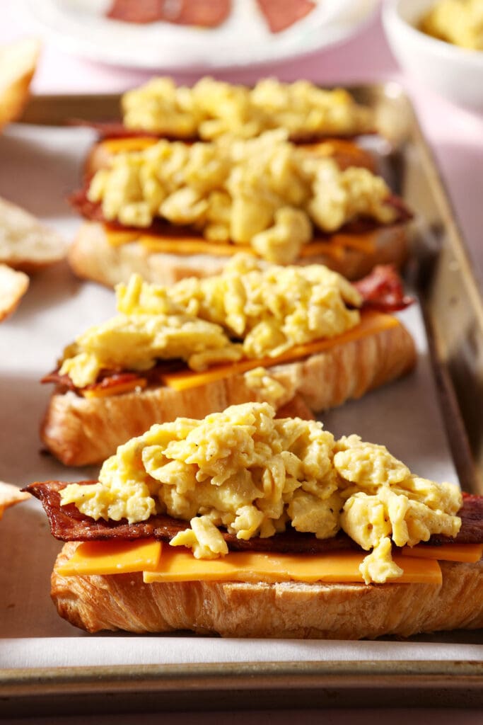 scrambled eggs on top of other ingredients to make a breakfast sandwich on a sheet pan