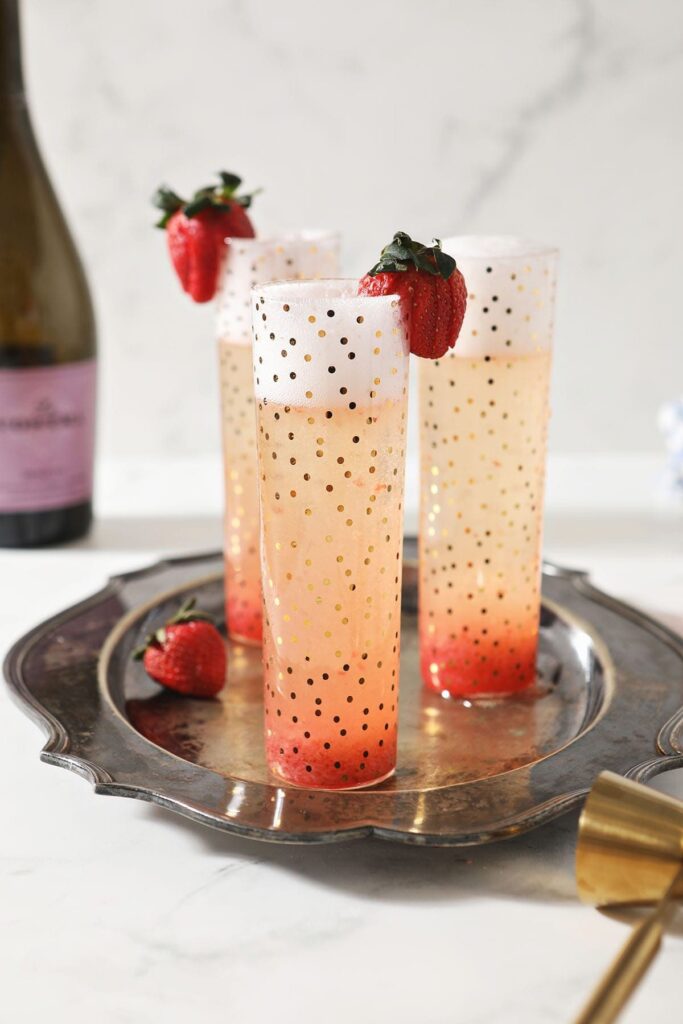 Three Strawberry Champagne Cocktails sit on a silver platter, garnished with fresh strawberries