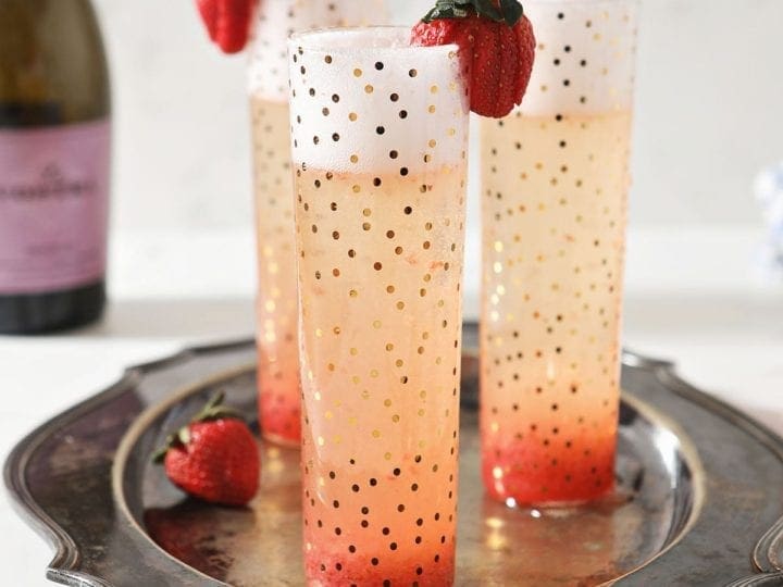 Three Strawberry Champagne Cocktails sit on a silver platter, garnished with fresh strawberries
