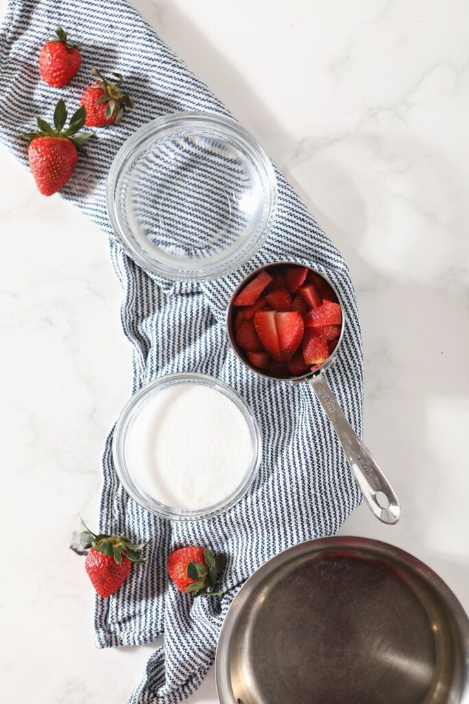 Ingredients for strawberry simple syrup in measuring cups on a blue striped towel