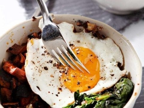 A fork piercing an egg yolk on top of curried veggie rice bowl