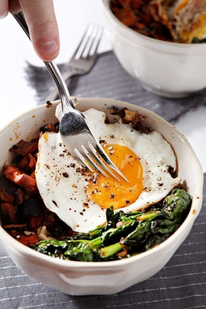 A fork piercing an egg yolk on top of curried veggie rice bowl 